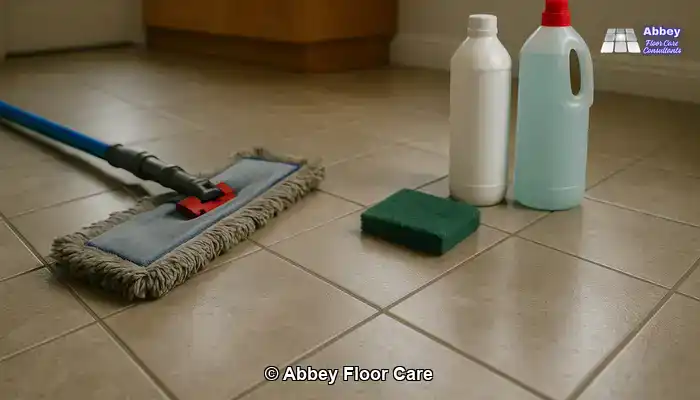 Dull tiled kitchen floor with dark grout and generic DIY cleaning tools beside it, showing limited improvement from home methods.